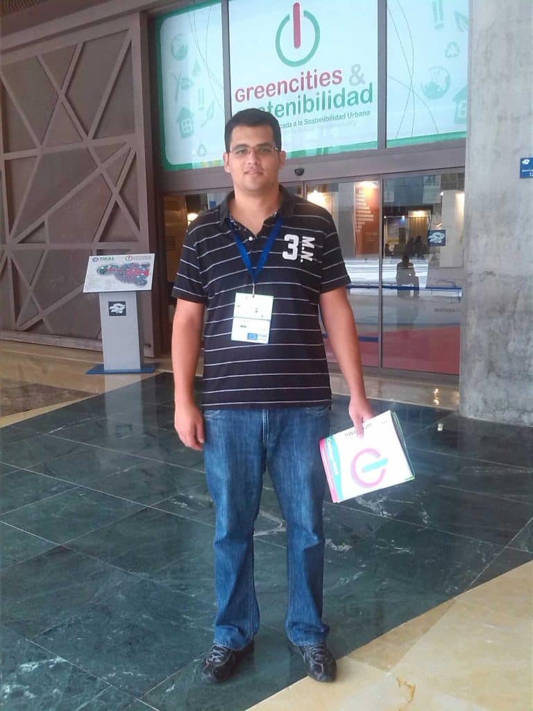 Asistente de Métrica6 en la entrada del Foro Greencities y Sostenibilidad Málaga 2013 con cartel del evento en el FYCMA